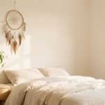 Où placer un attrape-rêves dans une chambre sans l’alourdir Attrape-rêves délicat suspendu au-dessus d'une table de chevet dans une chambre minimaliste lumineuse, avec literie claire, bois naturel et espace visuel aéré.
